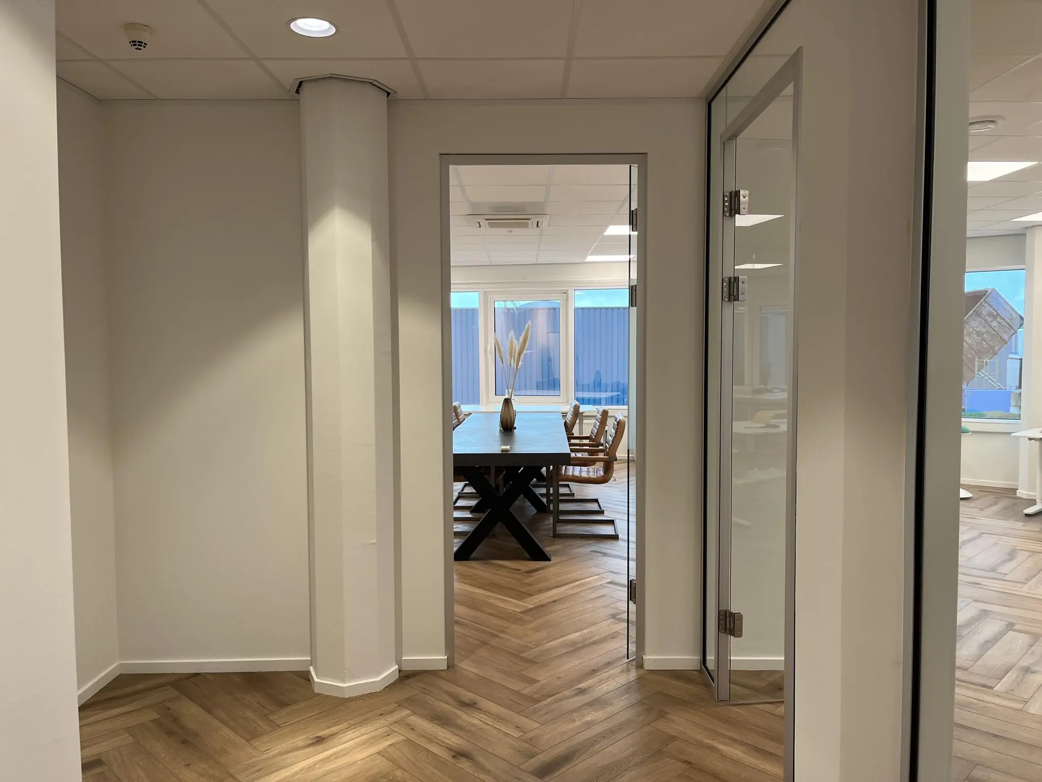 Doorkijk naar een moderne vergaderruimte met houten visgraatvloer en glazen deur in een kantoor aan de Lange Dreef.